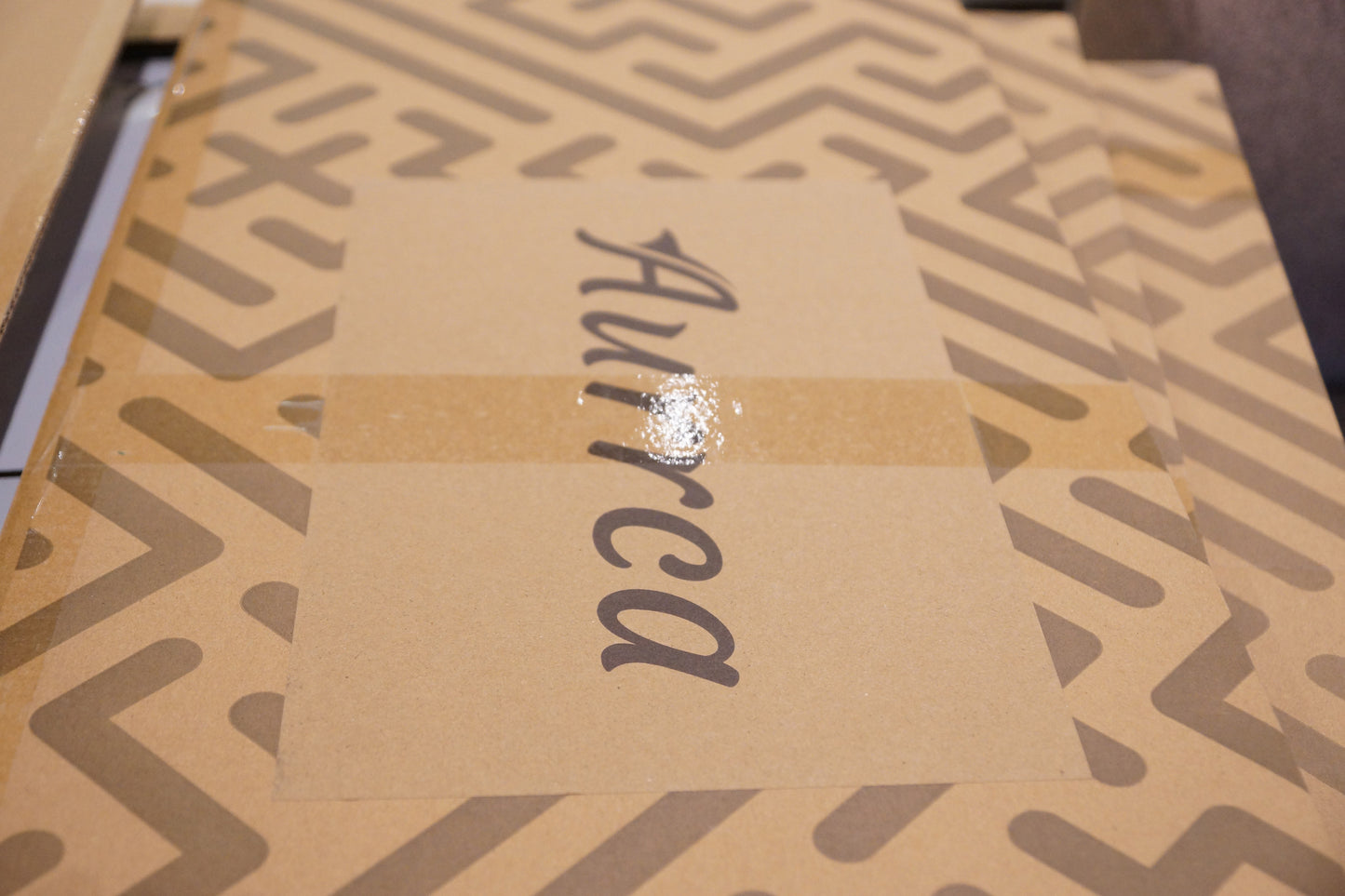 Stacked Aurrca kraft packaging boxes with geometric print and logo, used for securely shipping premium metal posters.